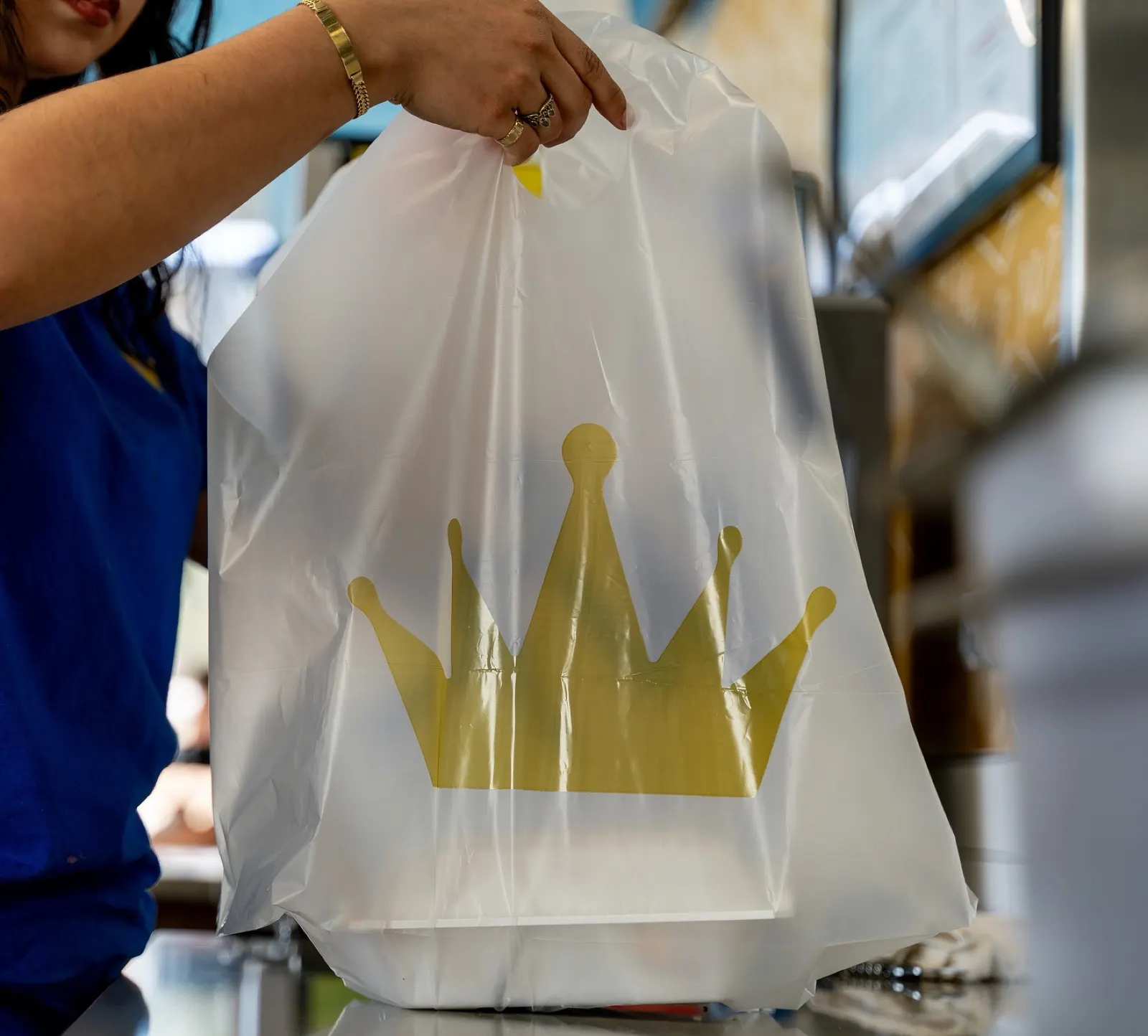A Wing Kings crew member lifting a gold-crown takeout bag across the counter